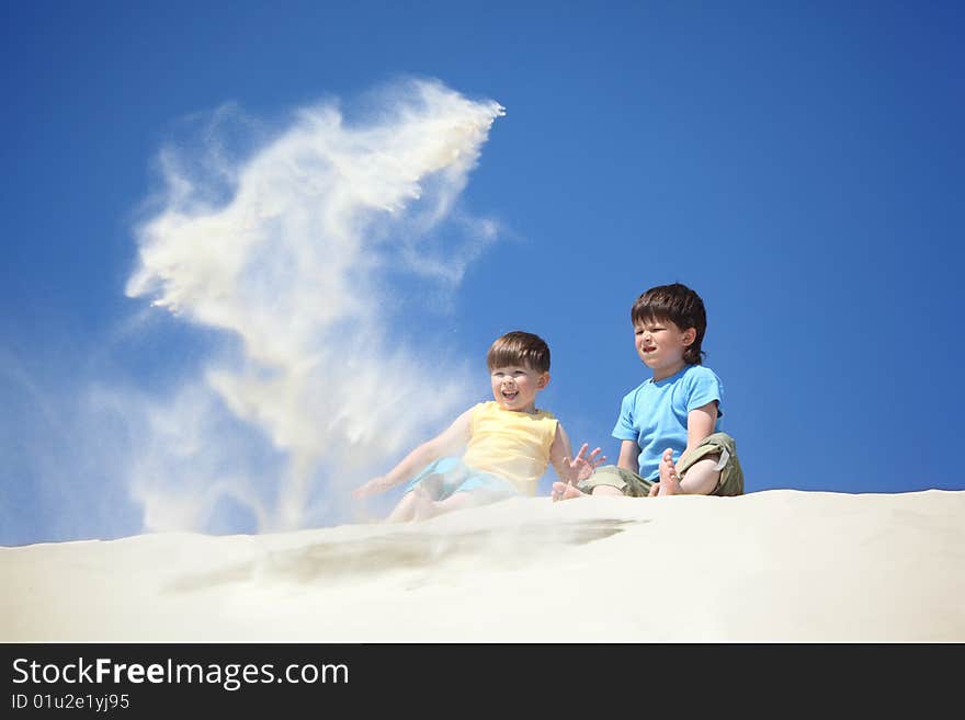 Two boys sit on sand and scatter it, summer day