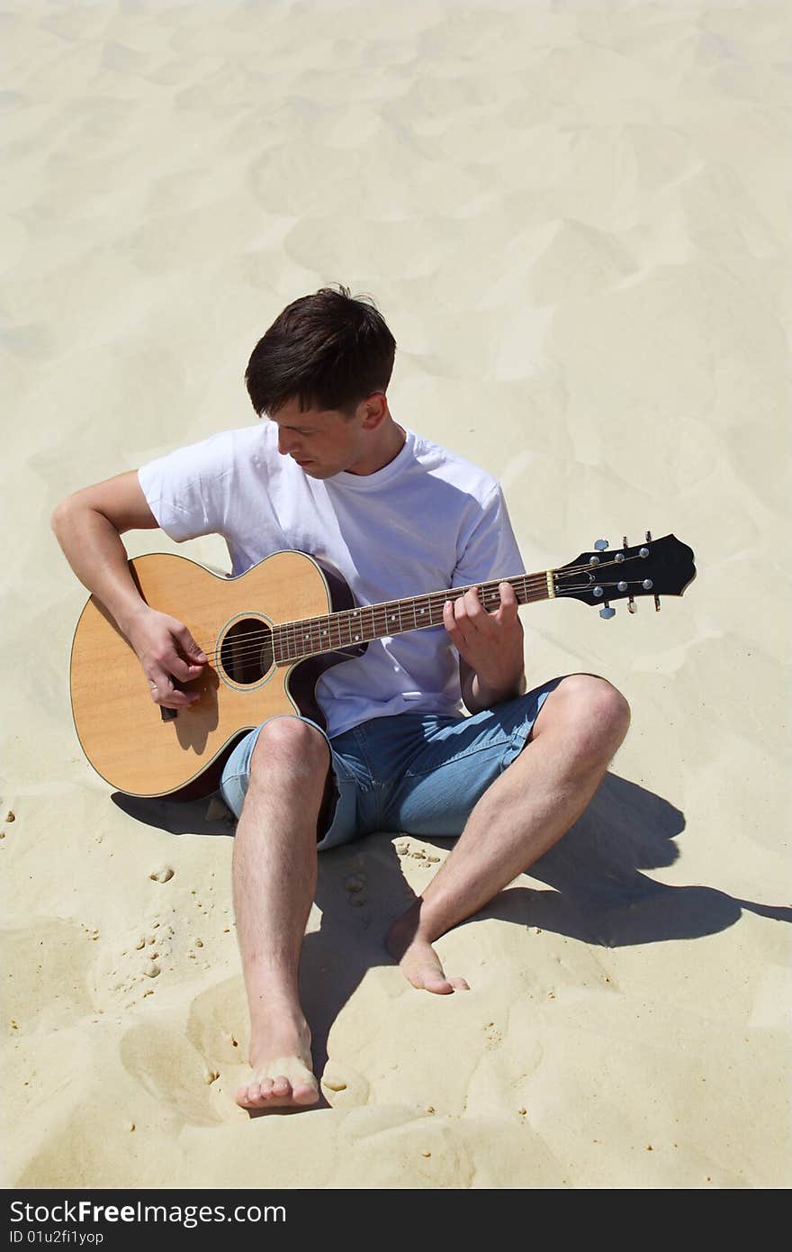 Guy plays guitar sitting on sand, summer day