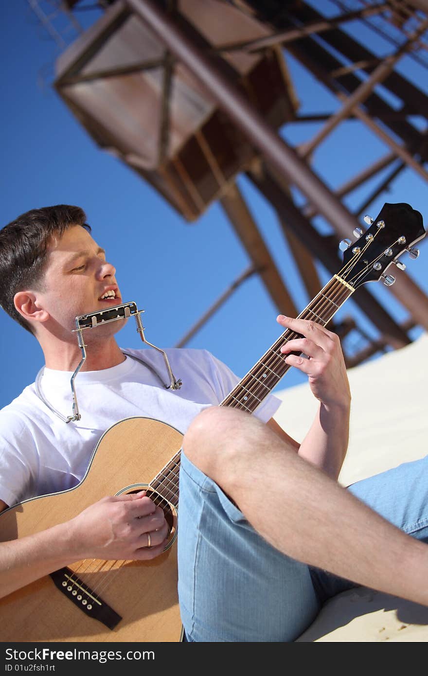 Guy plays guitar and lip accordion sitting on sand. Guy plays guitar and lip accordion sitting on sand