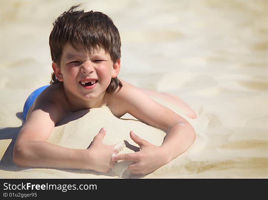 Boy without  foreteeth lies on sand