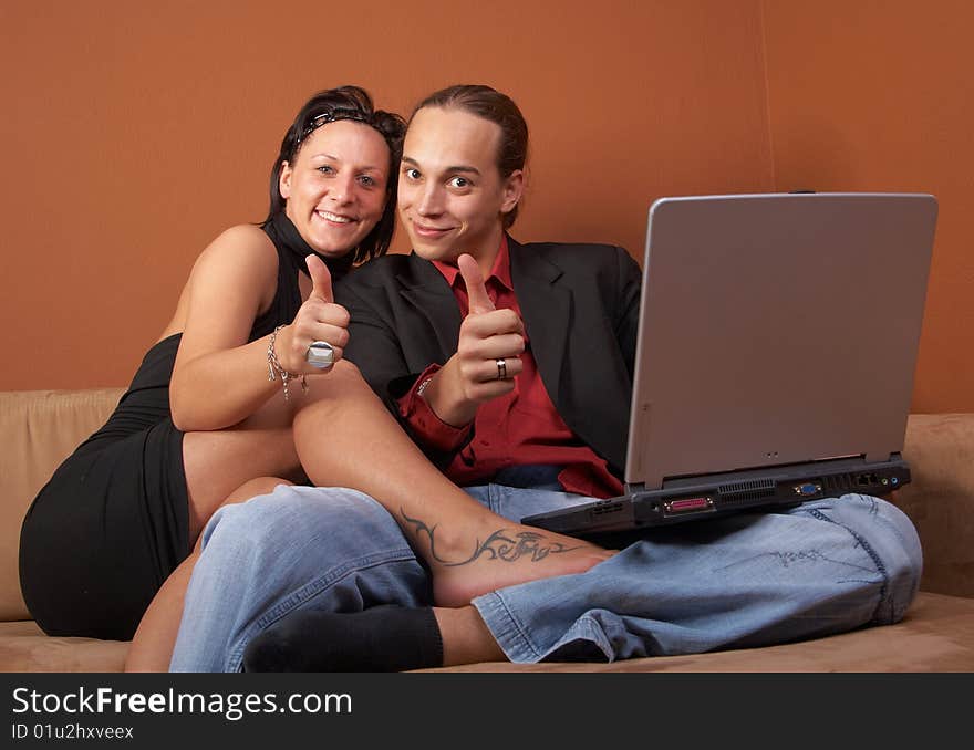 Young couple on the couch surfing the web with their laptop - showing a thumbs up sign. Young couple on the couch surfing the web with their laptop - showing a thumbs up sign.