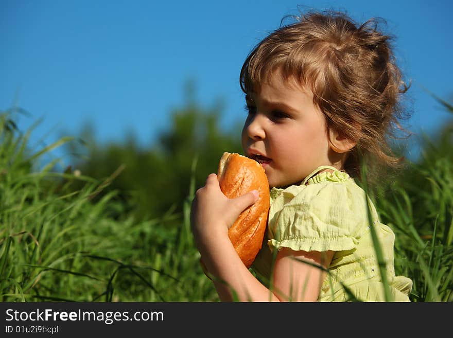 Girl eats bread in grass against blue sky