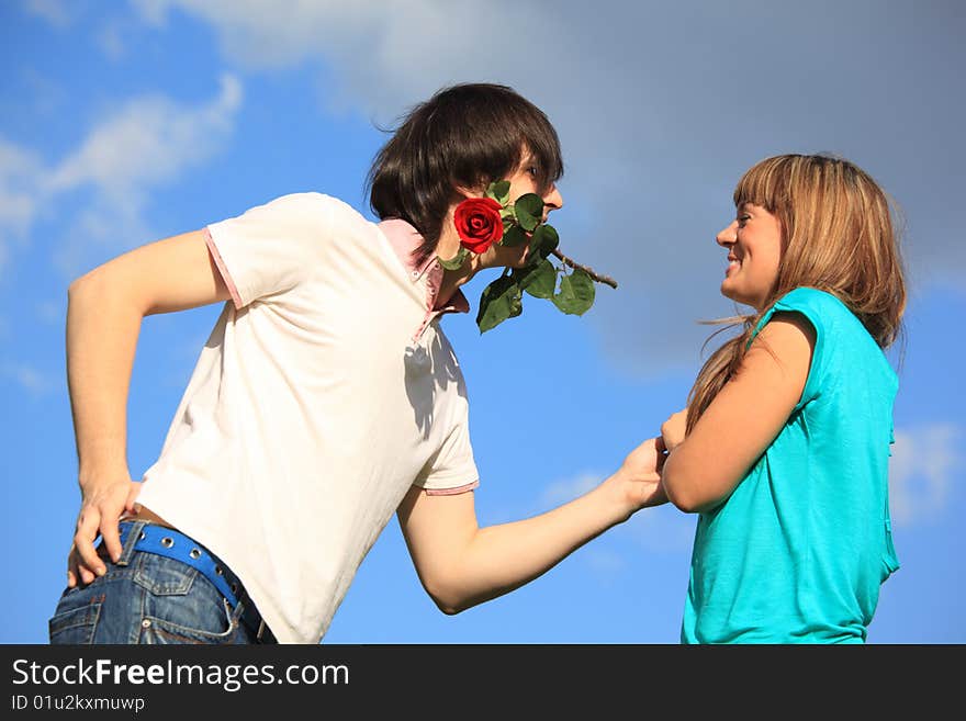 Guy with rose in mouth and smiling girl against sky. Guy with rose in mouth and smiling girl against sky