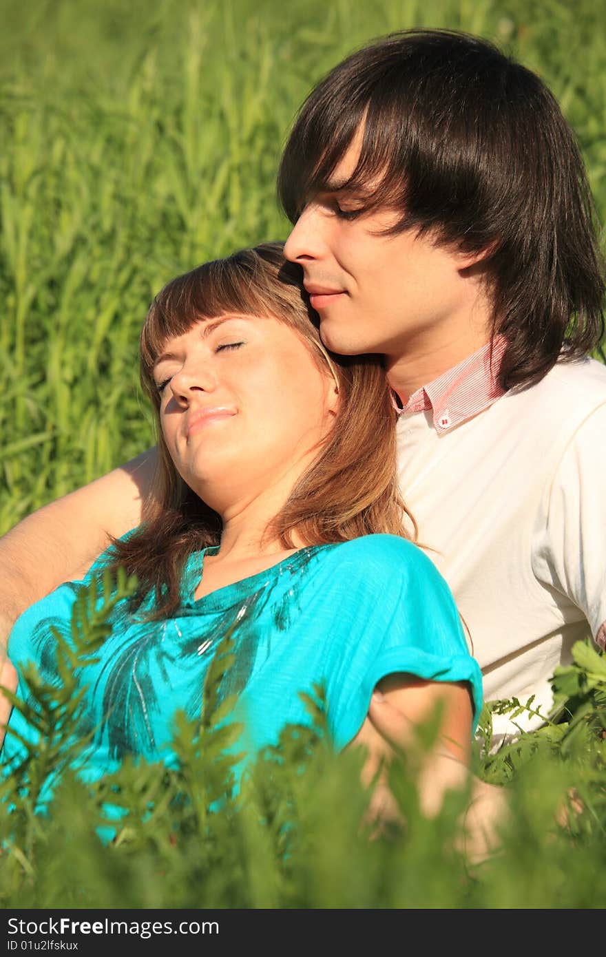 Girl lies on guy sitting in green grass. Girl lies on guy sitting in green grass