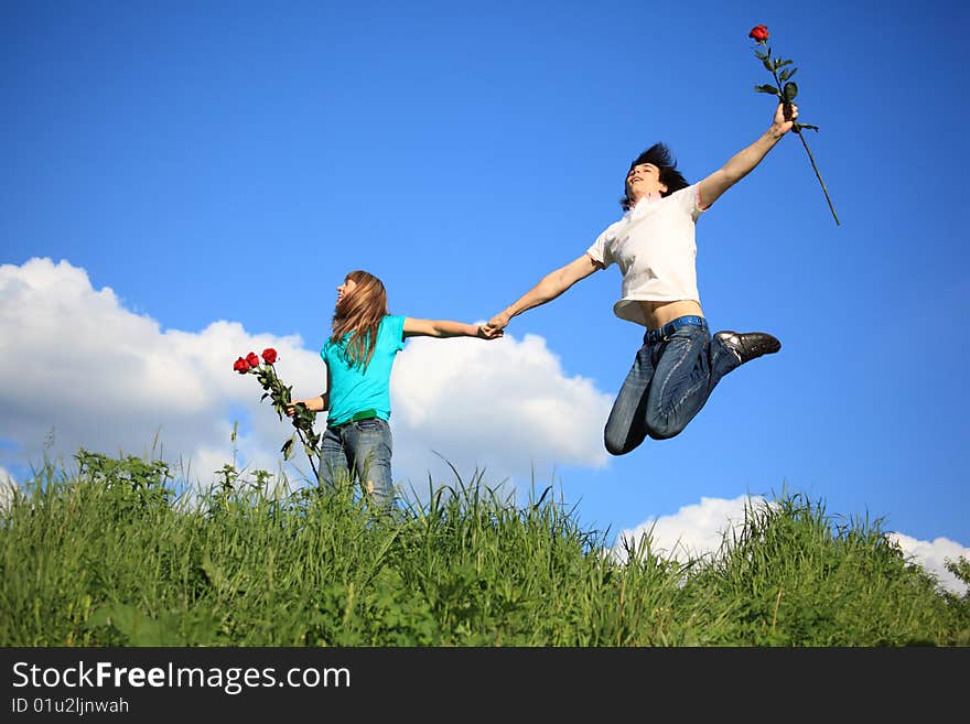 Guy with rose jumps holding girl with roses by hand. Guy with rose jumps holding girl with roses by hand