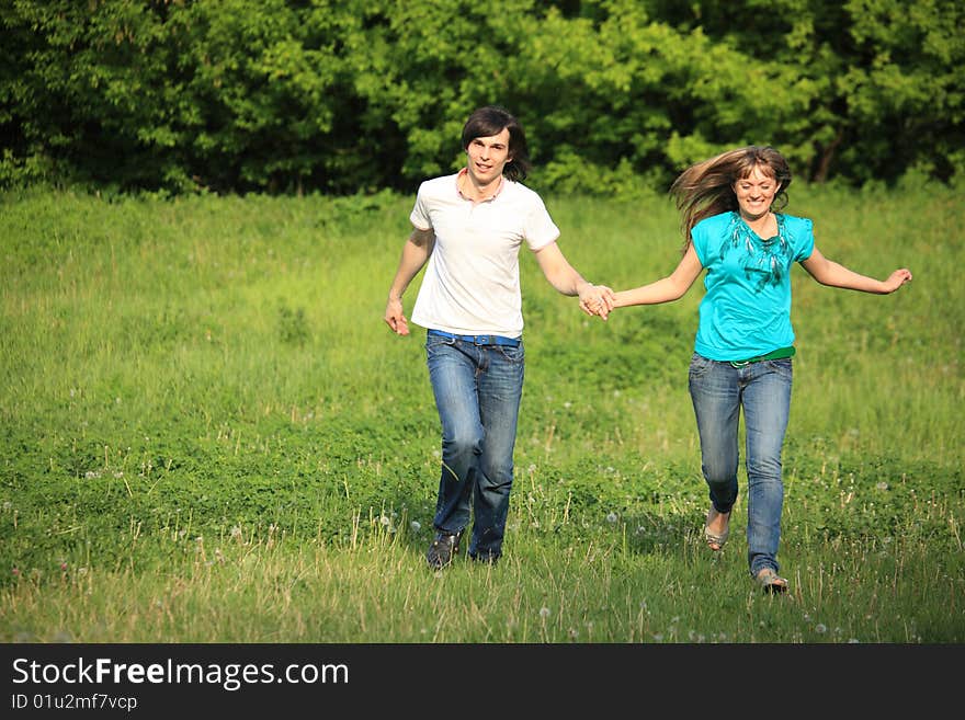 Young pair runs, keeping for hands, on grass in park. Young pair runs, keeping for hands, on grass in park