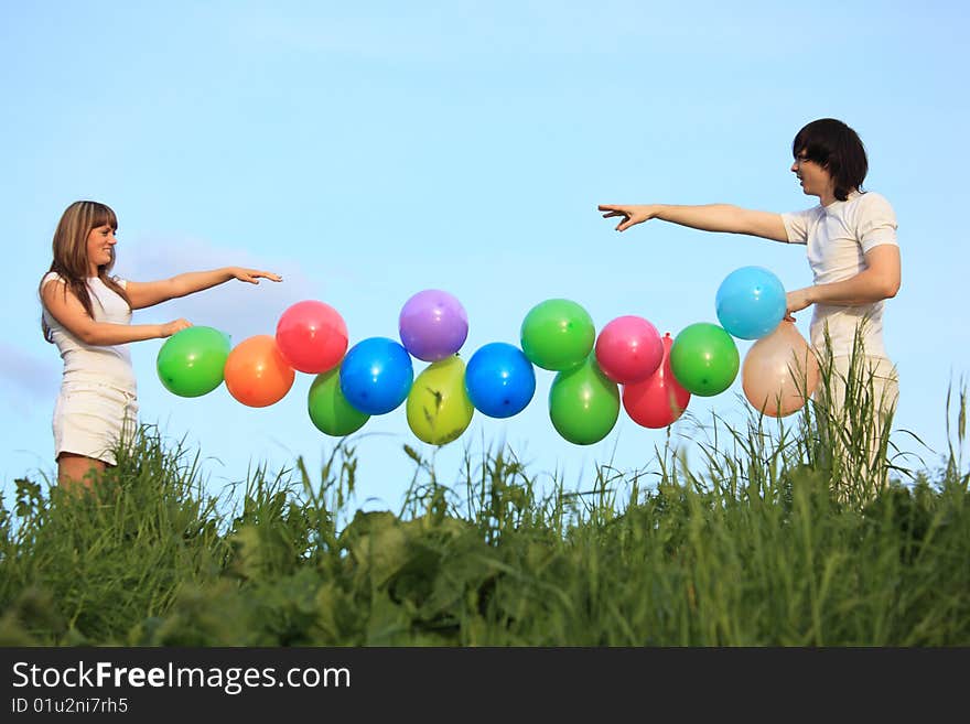 Girl and guy hold garland of multicoloured balloons in grass against sky. Girl and guy hold garland of multicoloured balloons in grass against sky