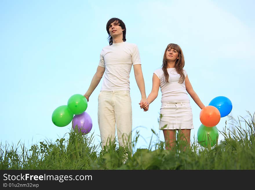 Girl and guy stand in grass with multicoloured balloons in hands. Girl and guy stand in grass with multicoloured balloons in hands