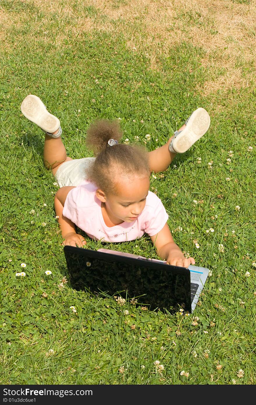 Beautiful young mixed race girl using laptop on a field of green grass and daisy wheel and clovers. She has the expression of contemplating what she is looking at on the display as she surfs the internet.