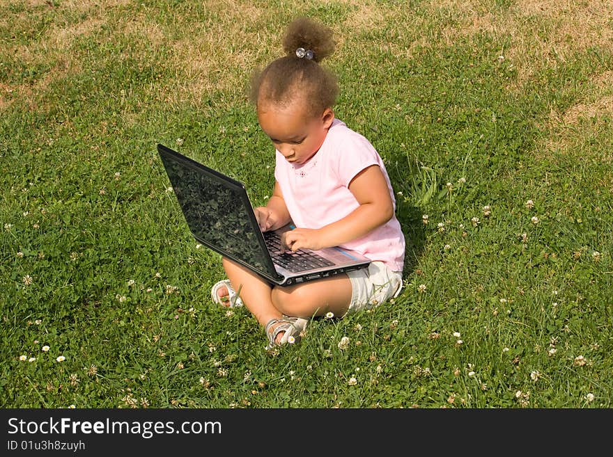 Beautiful young mixed race girl using laptop on a field of green grass and daisy wheel and clovers. She has the expression of contemplating what she is looking at on the display as she surfs the internet.