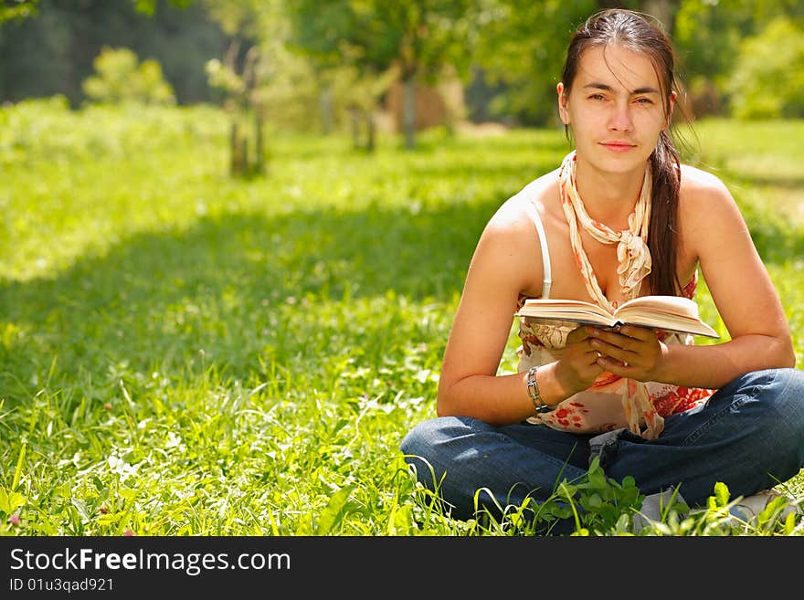 Young attractive woman reading a book and sitting on a grass