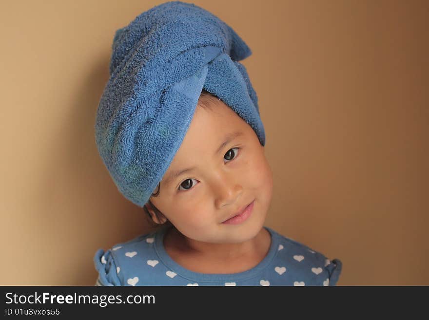 Closeup of a little girl of Asian descent, her hair wrapped in a blue bath towel. Isolated against a beige background. Closeup of a little girl of Asian descent, her hair wrapped in a blue bath towel. Isolated against a beige background.