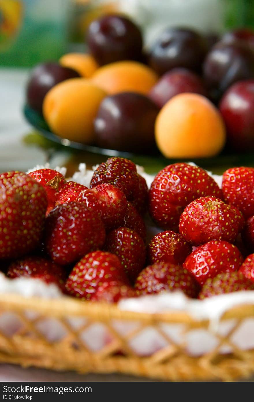 Close-up photo of strawberries foreground and plums with apricots background