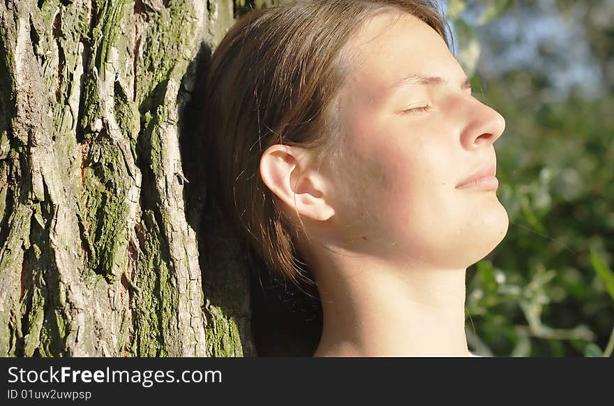 Girl with eyes closed leaned on the old tree with a ridge texture; young beautiful face with perfect springy skin. Girl with eyes closed leaned on the old tree with a ridge texture; young beautiful face with perfect springy skin