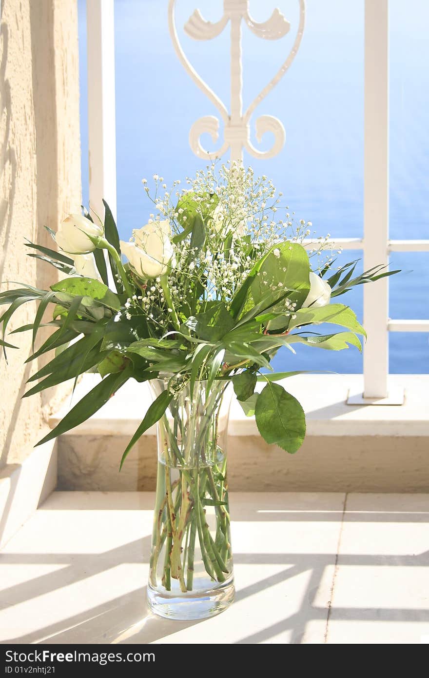 White roses in a glass vase, with blue morning sea on background