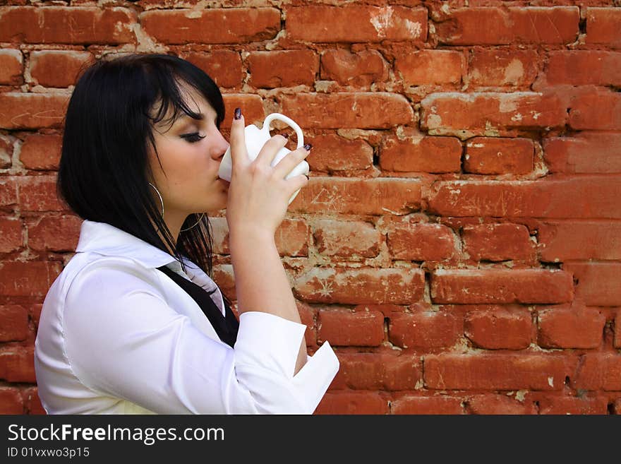 Young woman drinks from a cup on a background of a brick wall. Young woman drinks from a cup on a background of a brick wall