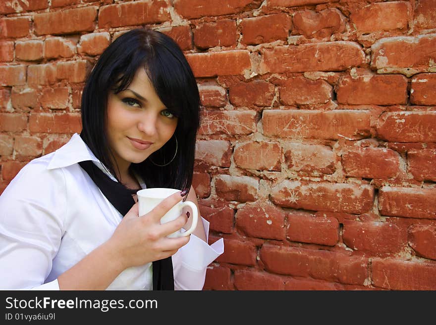 Young woman with a cup on a background of a brick wall. Young woman with a cup on a background of a brick wall