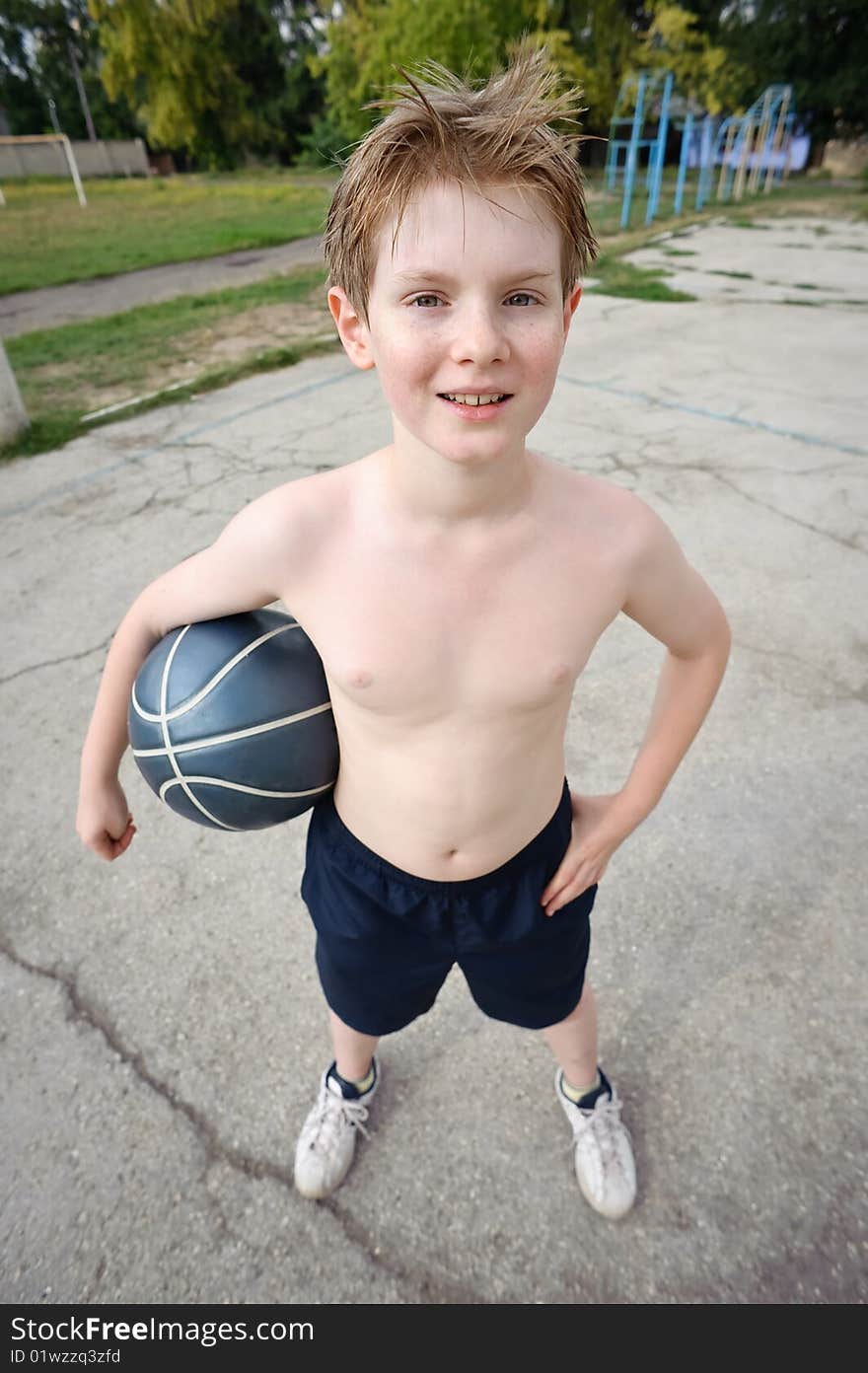 Happy boy plays basketball at school yard, looking at camera