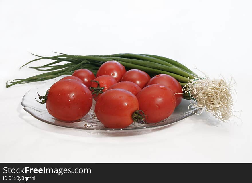 Fresh tomatoes and green salad onion with drops of water in a glass plate prepared for cooking. Fresh tomatoes and green salad onion with drops of water in a glass plate prepared for cooking.