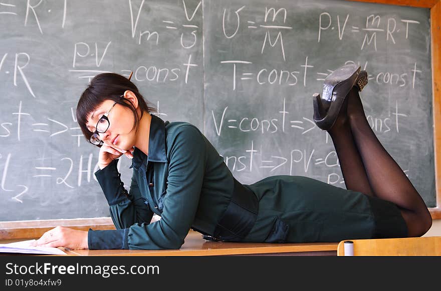 Beautiful student lays on a school desk near a blackboard