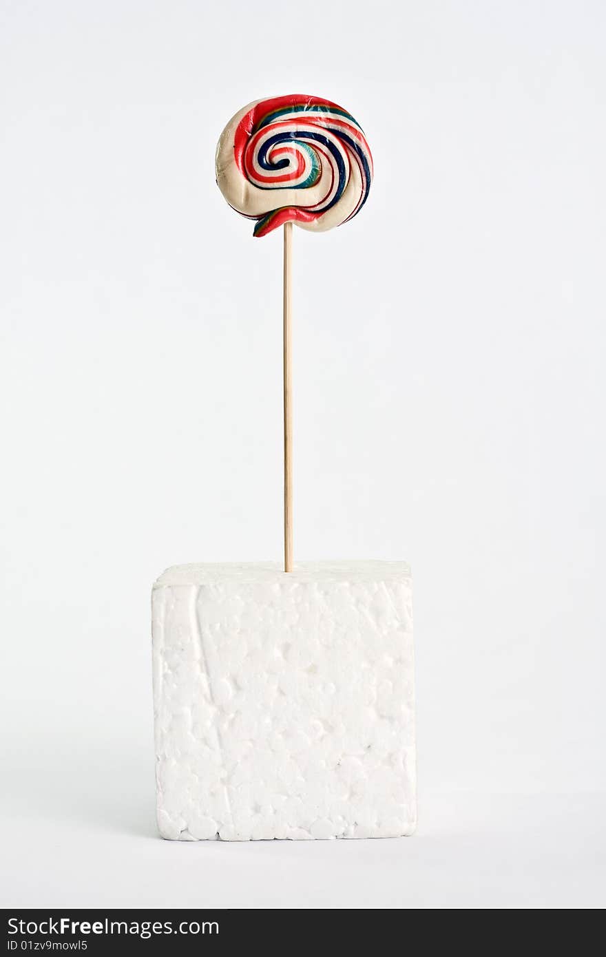 A colorful lollipop on white background supported on a polystyrene white cube. A colorful lollipop on white background supported on a polystyrene white cube