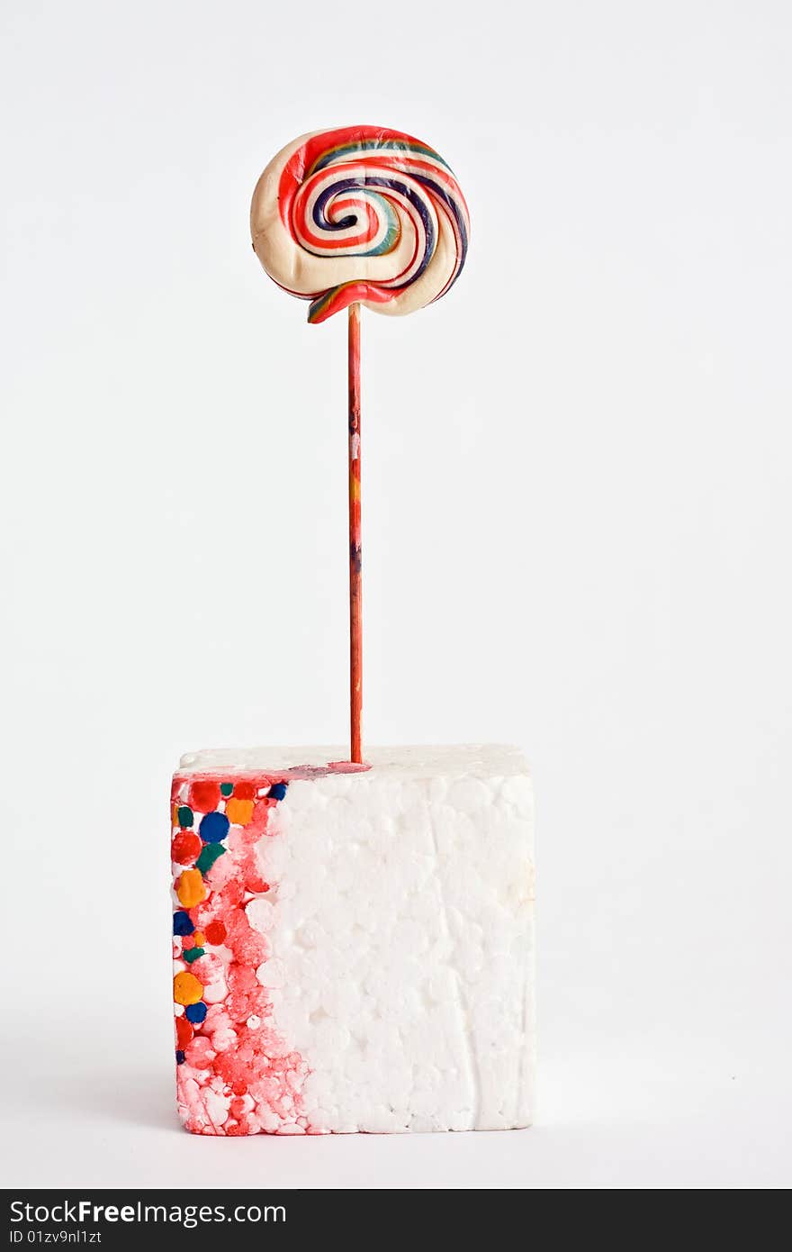 A lollipop that seems to melt and the colors trickle on a polystyrene cube. A lollipop that seems to melt and the colors trickle on a polystyrene cube