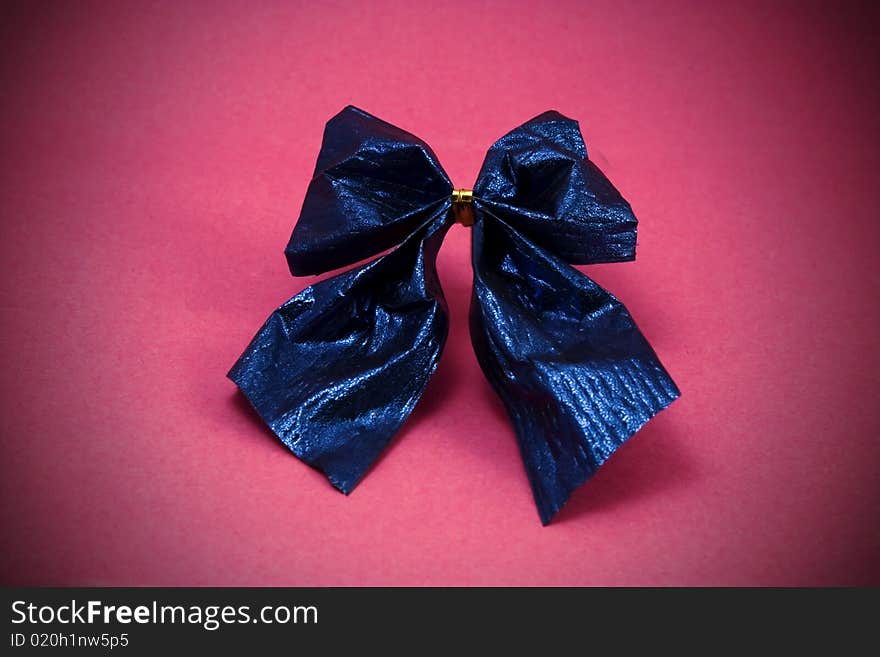 A macro picture of a shiny blue paper bow against a pink background