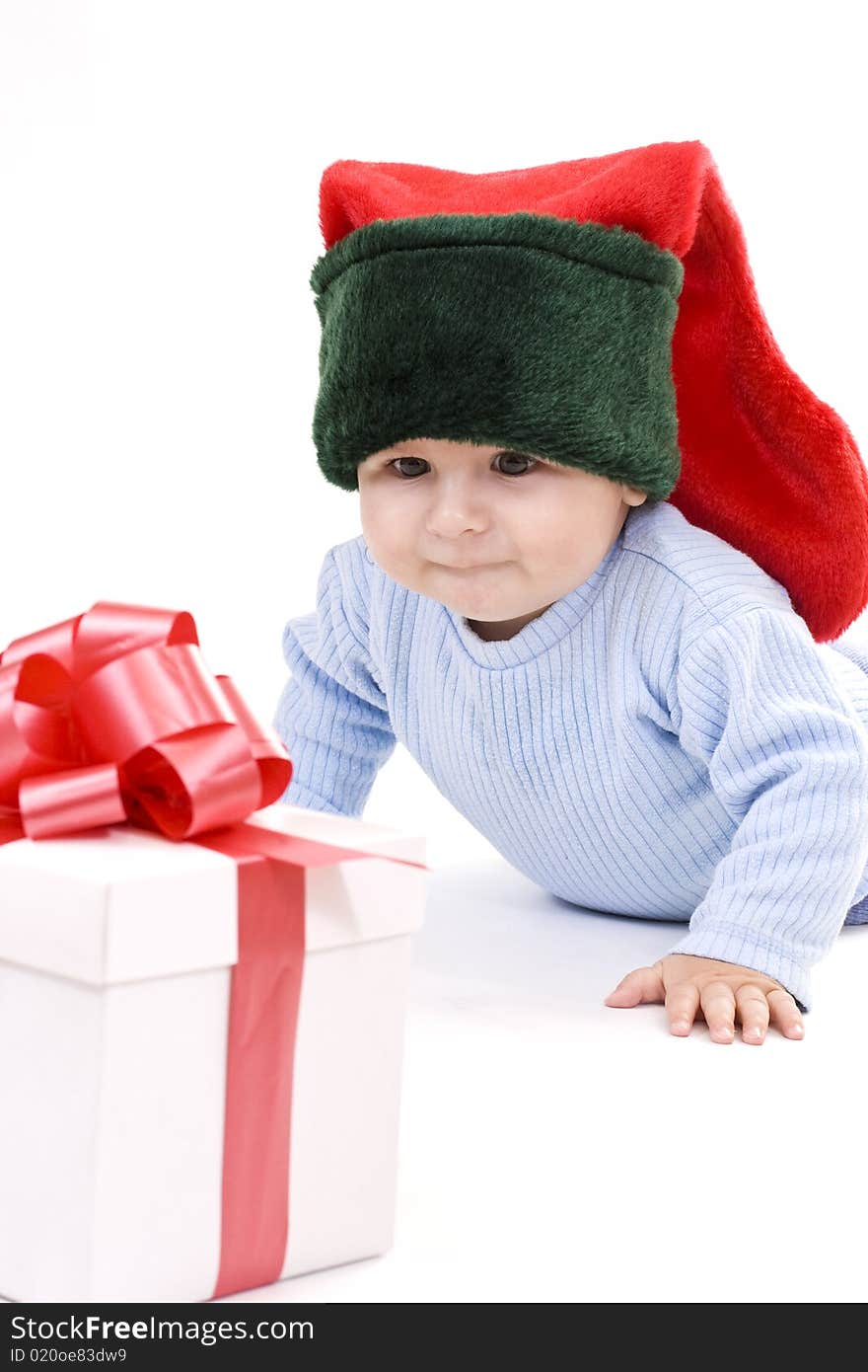 A baby wearing at elves hat looking at a gift. A baby wearing at elves hat looking at a gift