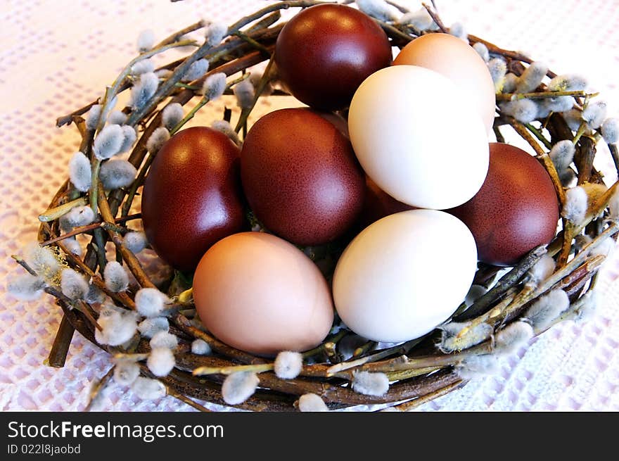 Easter dyed white, beige and chocolate eggs in a pussy-willow nest on a white lacy table-cloth, close up. Easter dyed white, beige and chocolate eggs in a pussy-willow nest on a white lacy table-cloth, close up