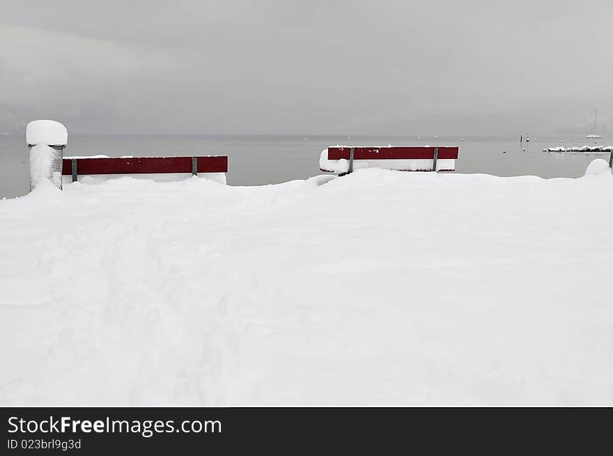 Red colored and deeply snow covered benches in front of Lake Thun. Red colored and deeply snow covered benches in front of Lake Thun