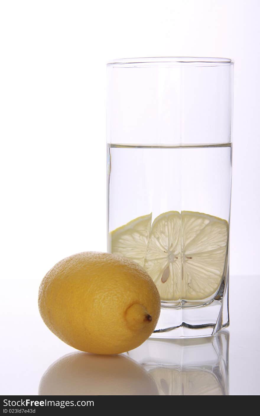 Glass with water and slice refreshing lemon on mirror table. Glass with water and slice refreshing lemon on mirror table