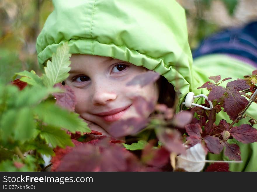 Smiling little girl hiding behind leaves