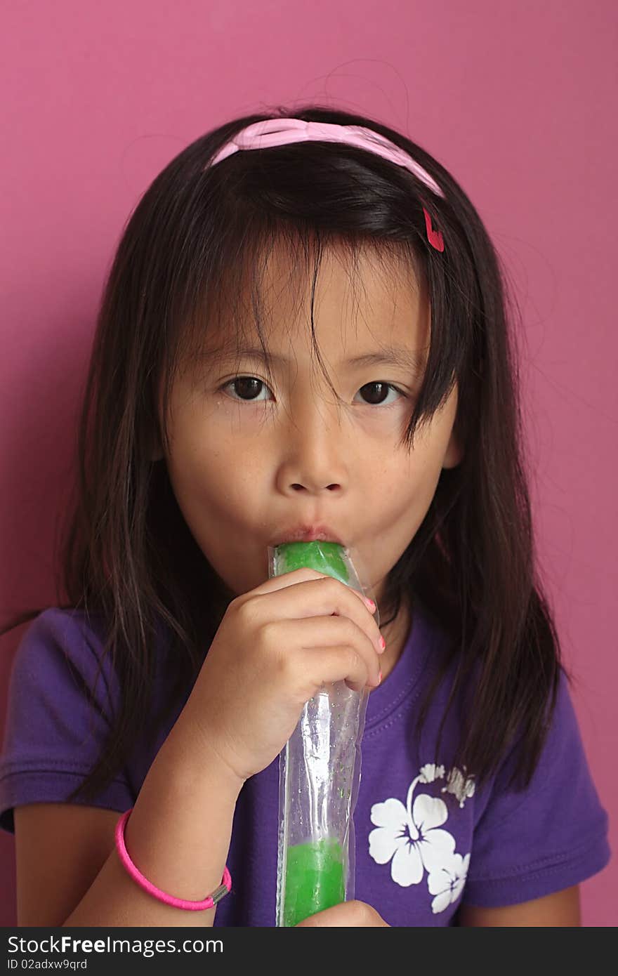 A happy little asian chinese girl eating an green ice pop. A happy little asian chinese girl eating an green ice pop