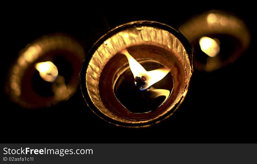 Closeup of three lit tea light candles burning with black background.