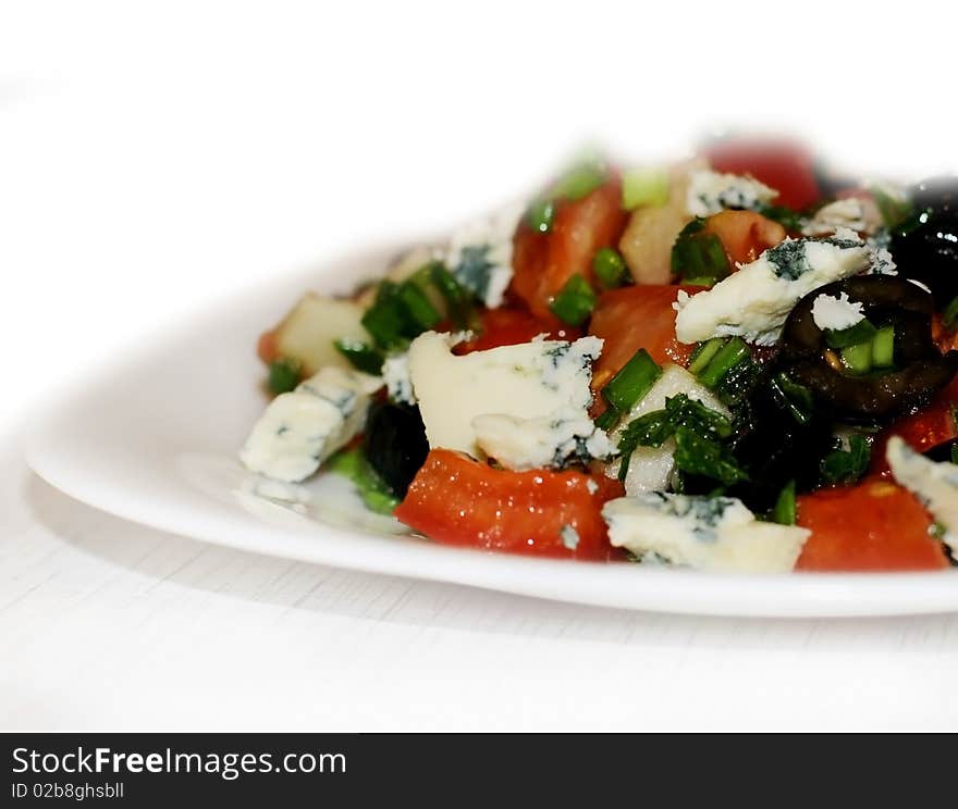 Salad with olives, tomatoes, green onion and blue cheese on a white plate