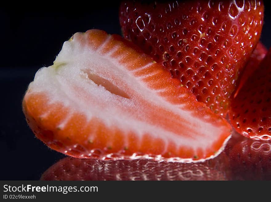 Closeup of whole and sliced strawberries reflecting on black background. Closeup of whole and sliced strawberries reflecting on black background.