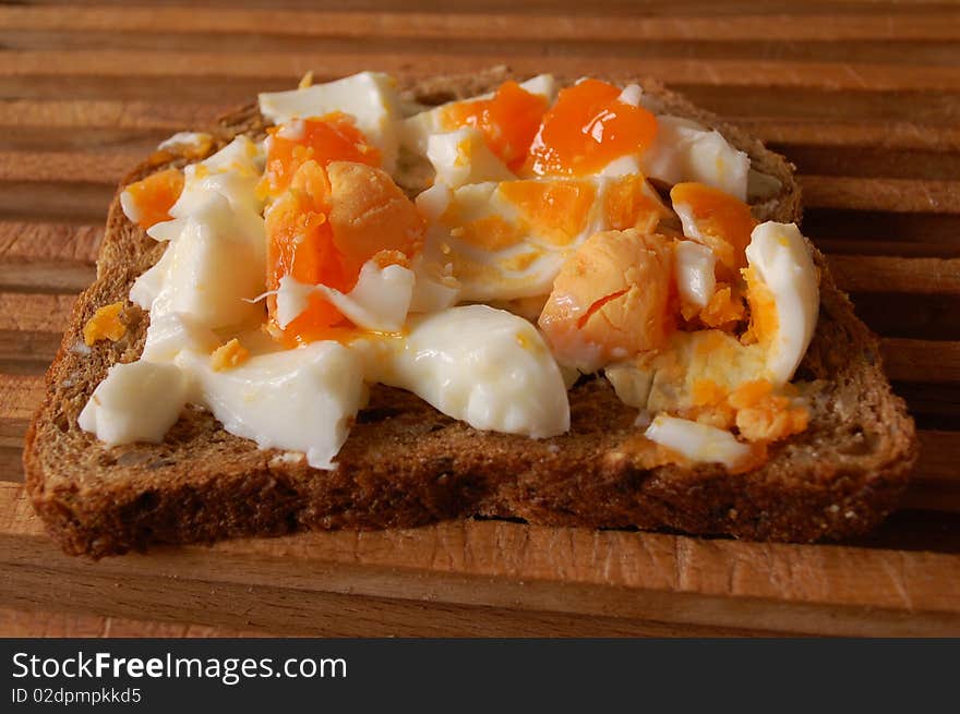 A brown sandwich with boiled eggs on a wooden plate. A brown sandwich with boiled eggs on a wooden plate