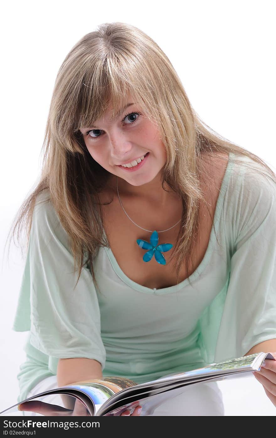 Young beautiful girl in it is light to a green blouse with the dismissed fair hair reads magazine in studio on a white background. Young beautiful girl in it is light to a green blouse with the dismissed fair hair reads magazine in studio on a white background