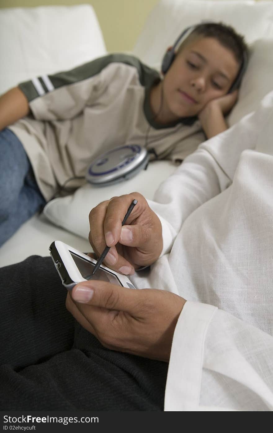 Father Using PDA on sofa with Son Listening to Music, close up of hands of father. Father Using PDA on sofa with Son Listening to Music, close up of hands of father