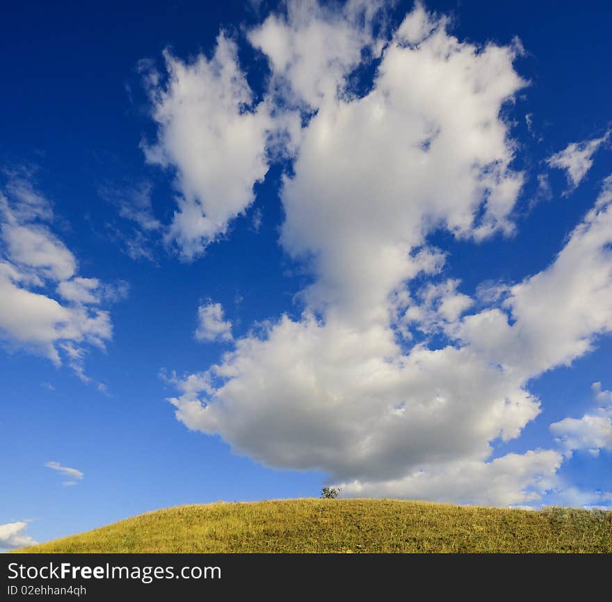 Landscape with white clouds on a background of the blue sky, a hill with a lonely tree. Landscape with white clouds on a background of the blue sky, a hill with a lonely tree