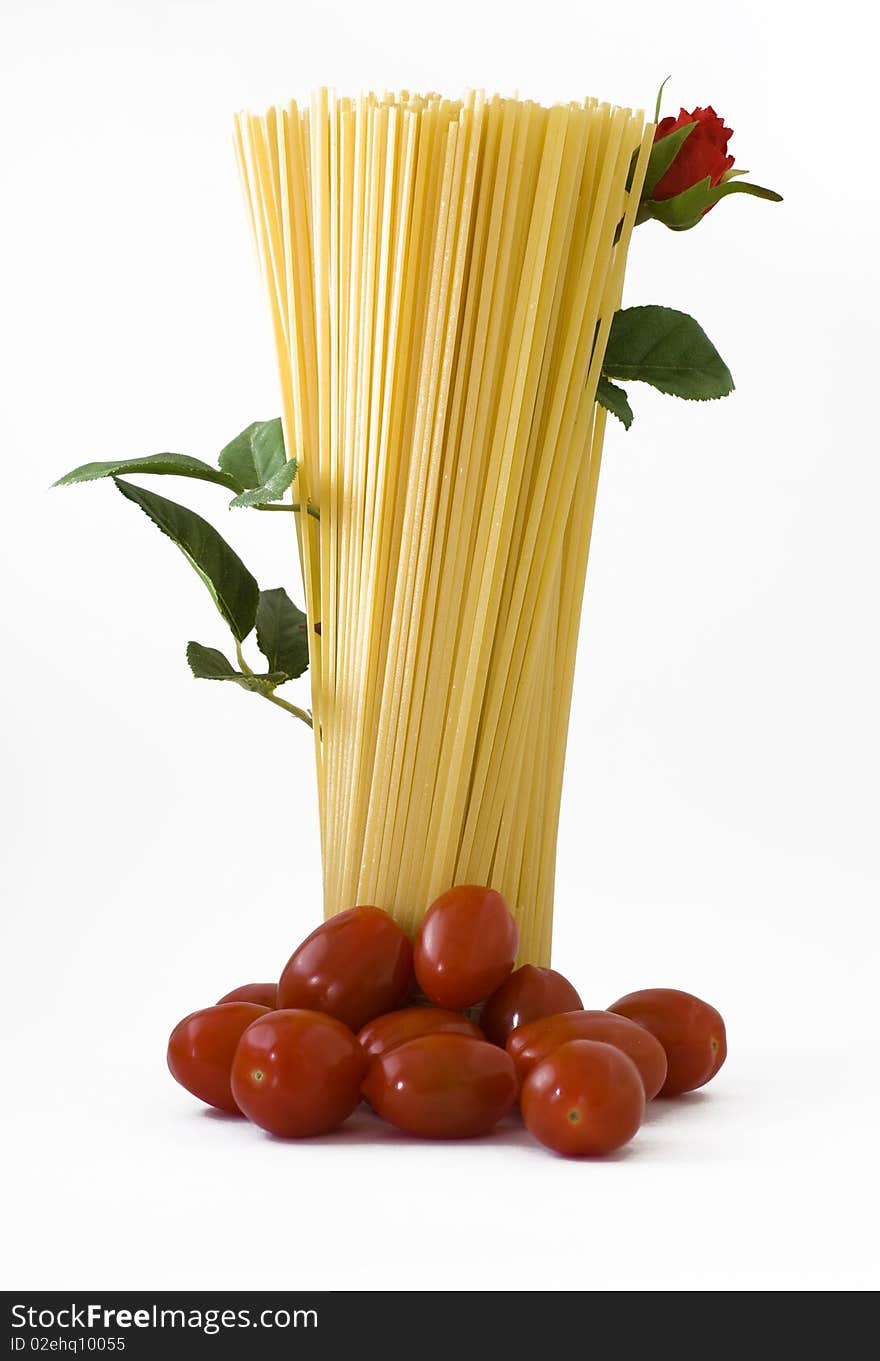 Raw spaghetti standing with tomatoes on the base and a flowered red rose up. Raw spaghetti standing with tomatoes on the base and a flowered red rose up