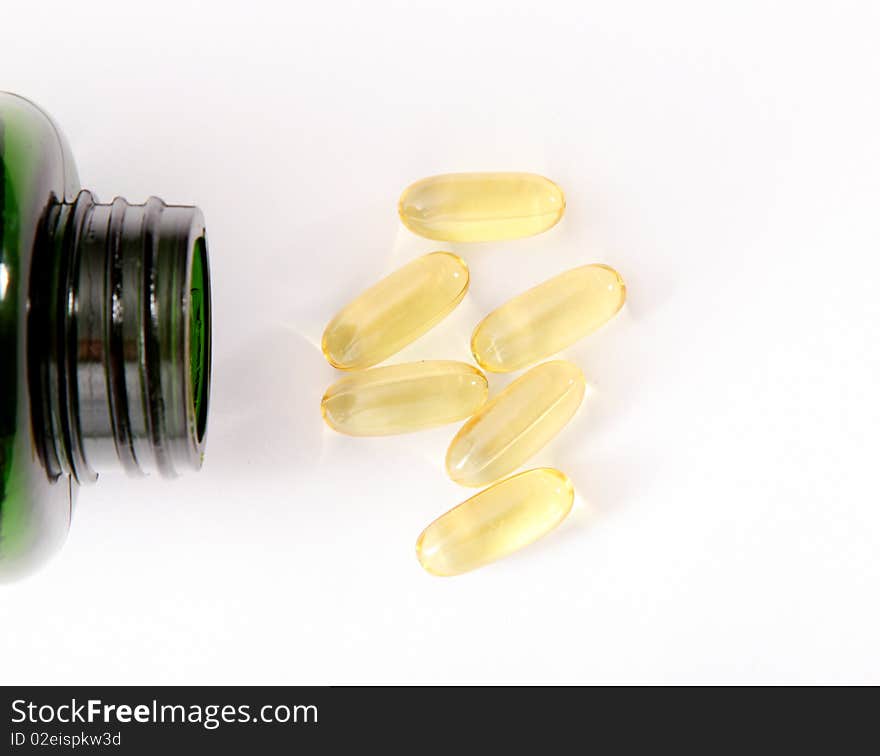 Yellow pills and green bottle on light background