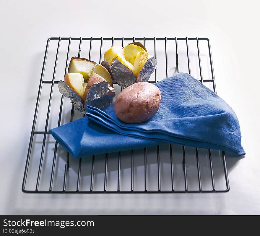 One whole and two jacket potatoes with blue serviette ,all on stainless steel grille.