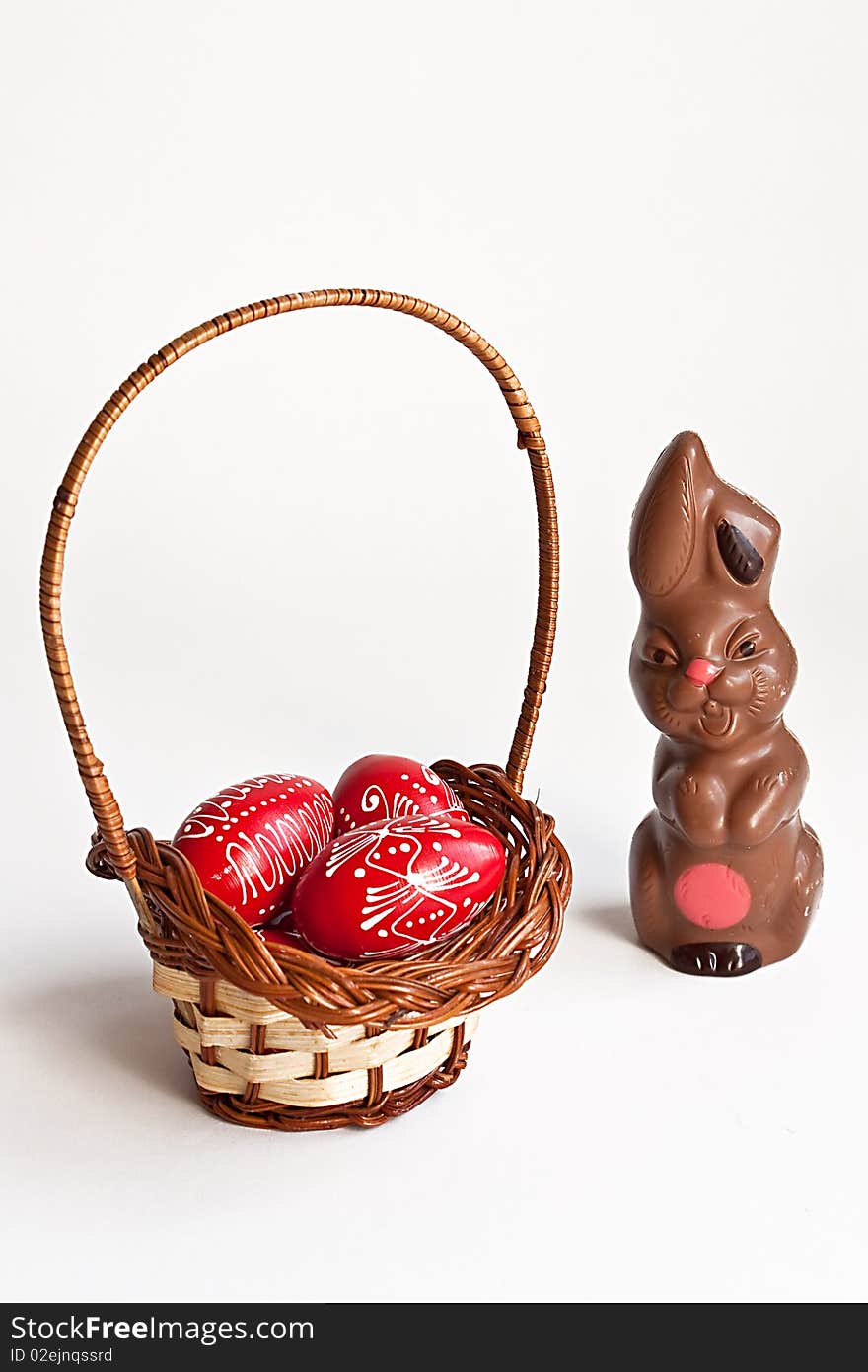 Milk chocolate bunny and red Easter eggs in a basket on white background. Milk chocolate bunny and red Easter eggs in a basket on white background