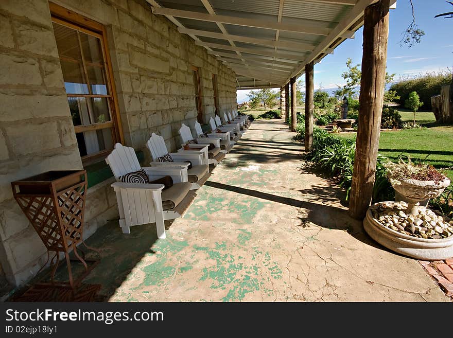 Perspective shot of many white wooden chairs on veranda of old stone building in shade to rest and relax. Perspective shot of many white wooden chairs on veranda of old stone building in shade to rest and relax