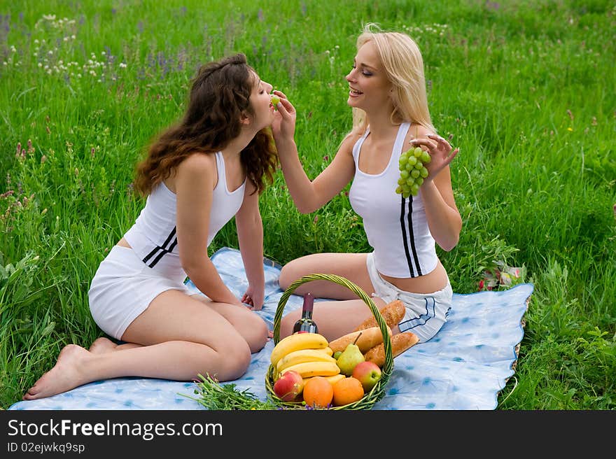 Two beautiful girls blonde and brunette in white suits, feed each other grapes. Two beautiful girls blonde and brunette in white suits, feed each other grapes