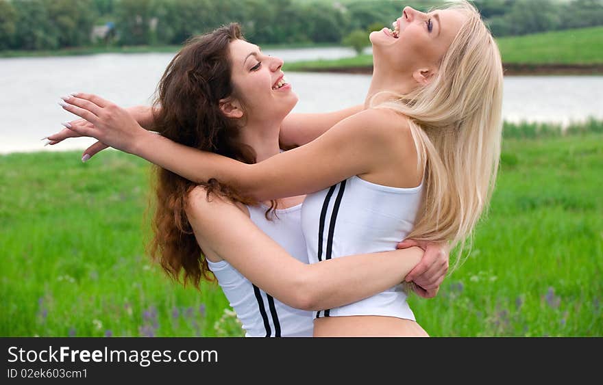 Two beautiful girls blonde and brunette in white suits, jump on the grass. Two beautiful girls blonde and brunette in white suits, jump on the grass