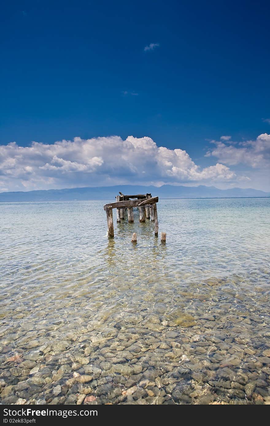 Decayed jetty in a lake blue skies clear water with pebbles