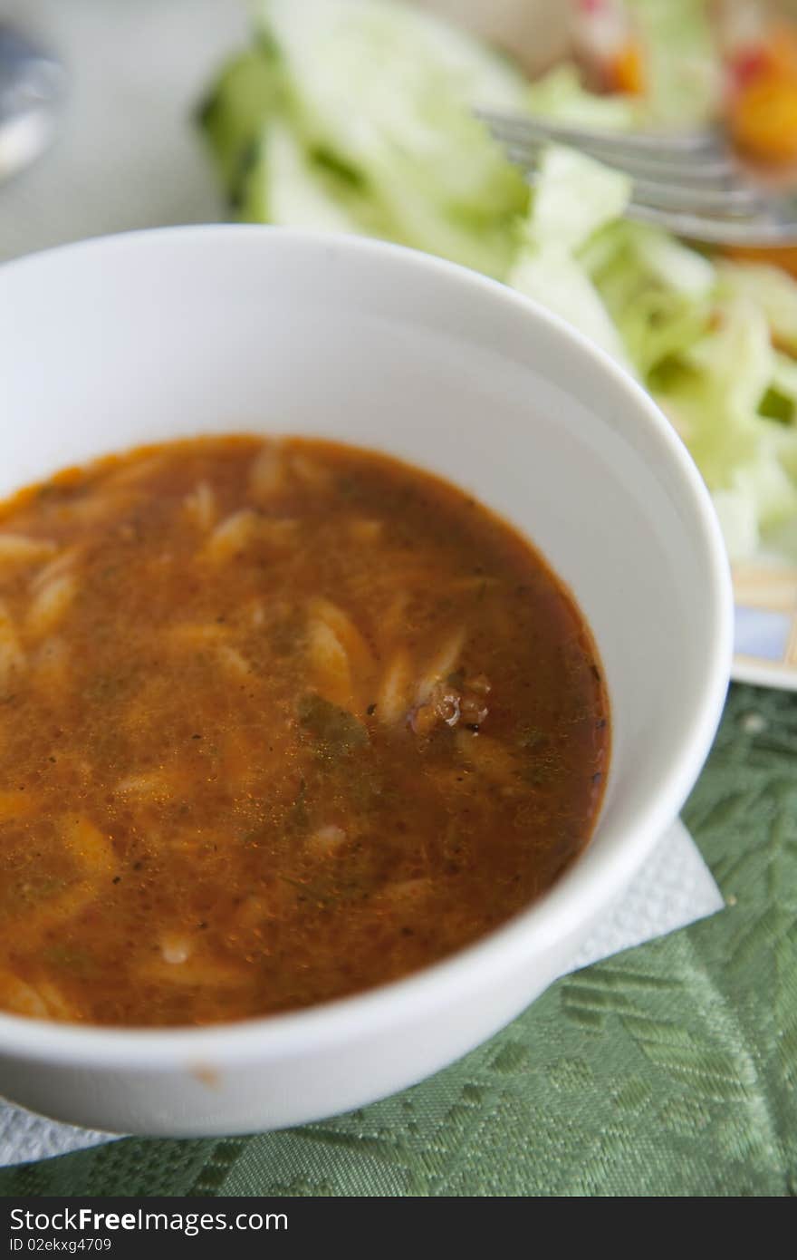 Spicy North African soup with noodles, vegetables and spices, with a side salad in the background. Spicy North African soup with noodles, vegetables and spices, with a side salad in the background.