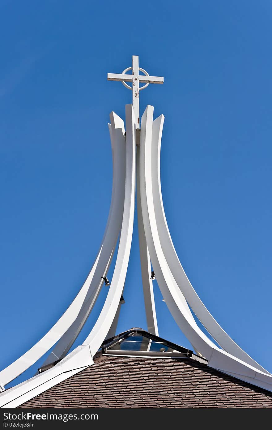 Under a clear blue sky, a cross is supported by curved beams on top of a church. Under a clear blue sky, a cross is supported by curved beams on top of a church.